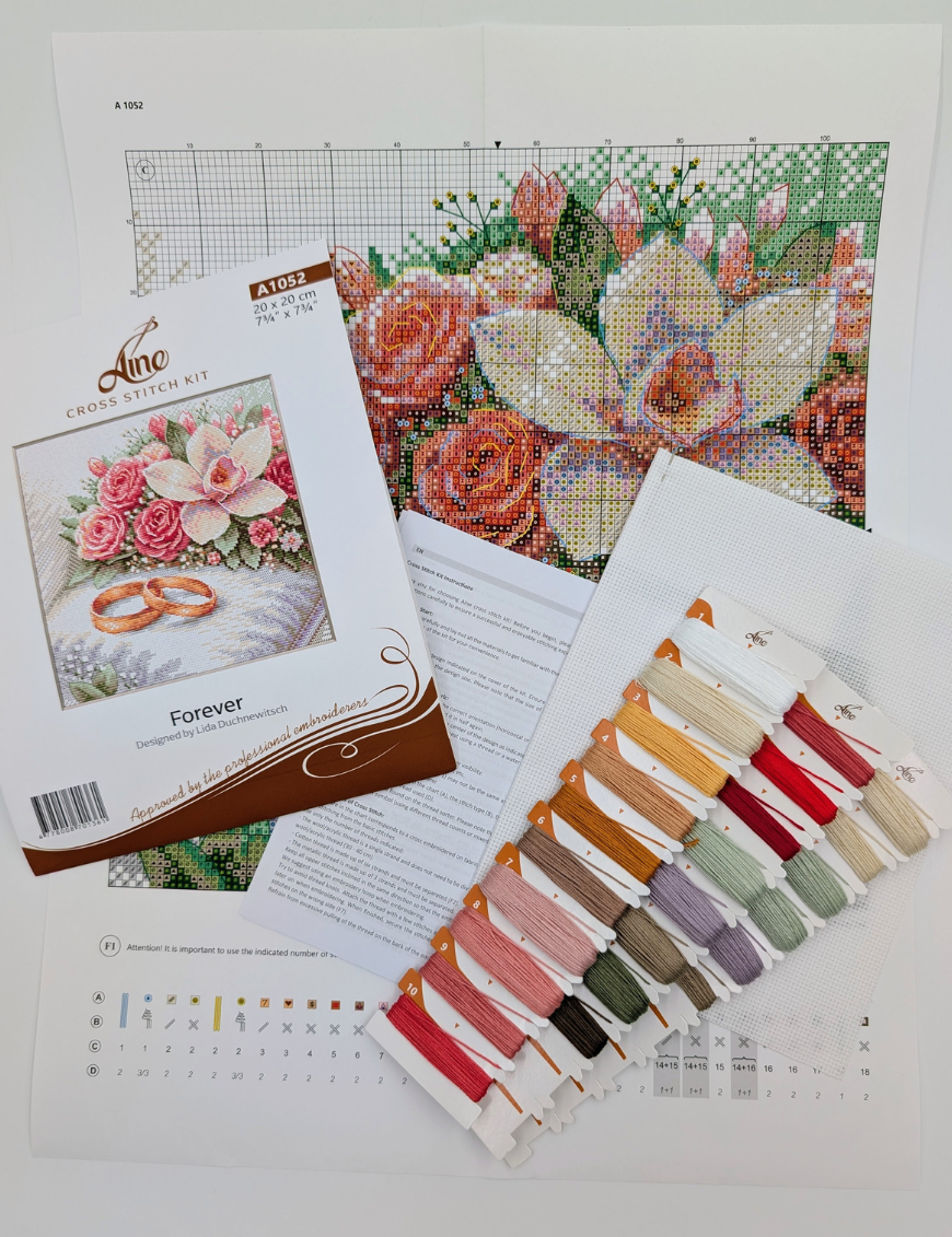 The A1052 Forever cross-stitch kit box laid out with the colour chart, instruction sheet, white Aida fabric and pre-sorted threads on numbered cards in pink, red, green, gold and purple shades.