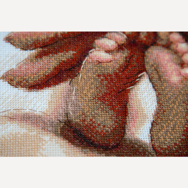Close-up of cross-stitched baby feet resting in a parent’s hand, showing the shading in terracotta, peach and rose threads.
