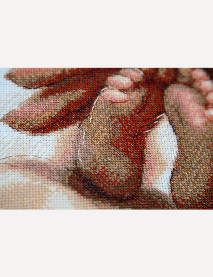 Close-up of cross-stitched baby feet resting in a parent’s hand, showing the shading in terracotta, peach and rose threads.